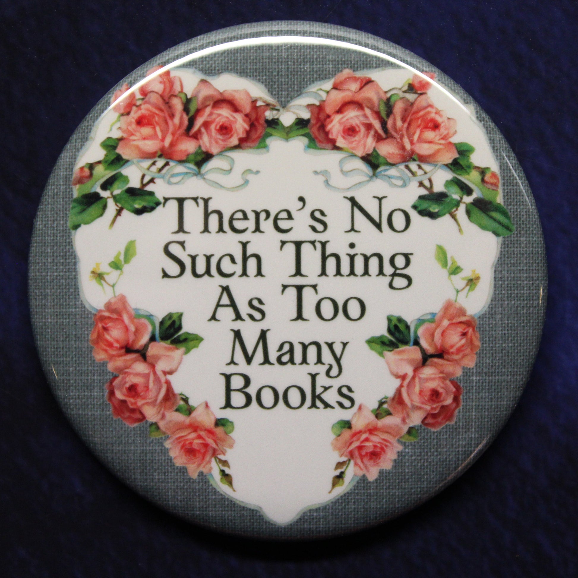 Round button badge with floral design and text 'There's No Such Thing As Too Many Books' on a dark background